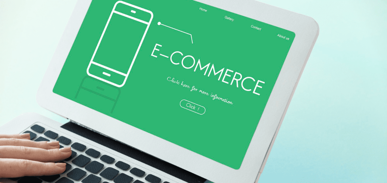 A person’s hand on a laptop keyboard with the screen displaying a green background and the word E-COMMERCE alongside a simple outline of a smartphone.